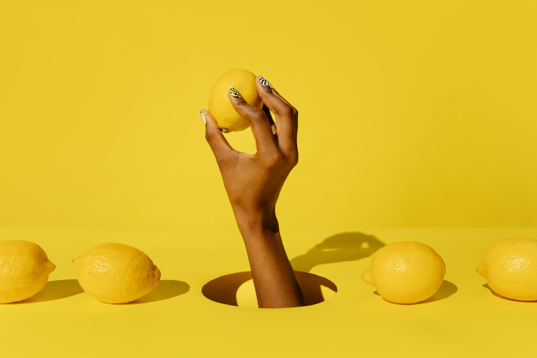 Hand holding a fresh lemon against a bright yellow background, symbolizing citrus freshness