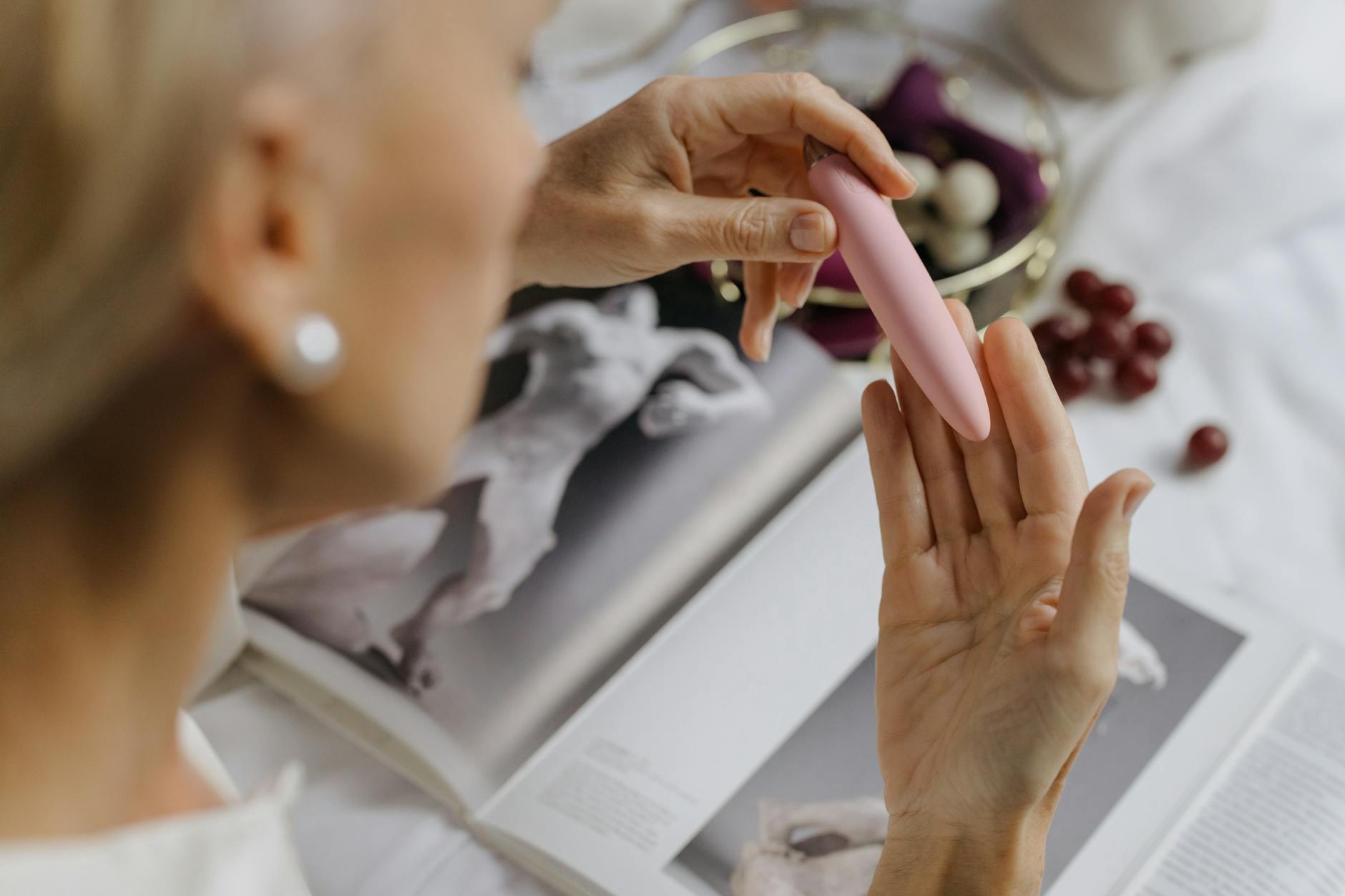 Close-up of a woman holding a pink vibrator with art books in the background, symbolizing personal rediscovery after heartbreak.