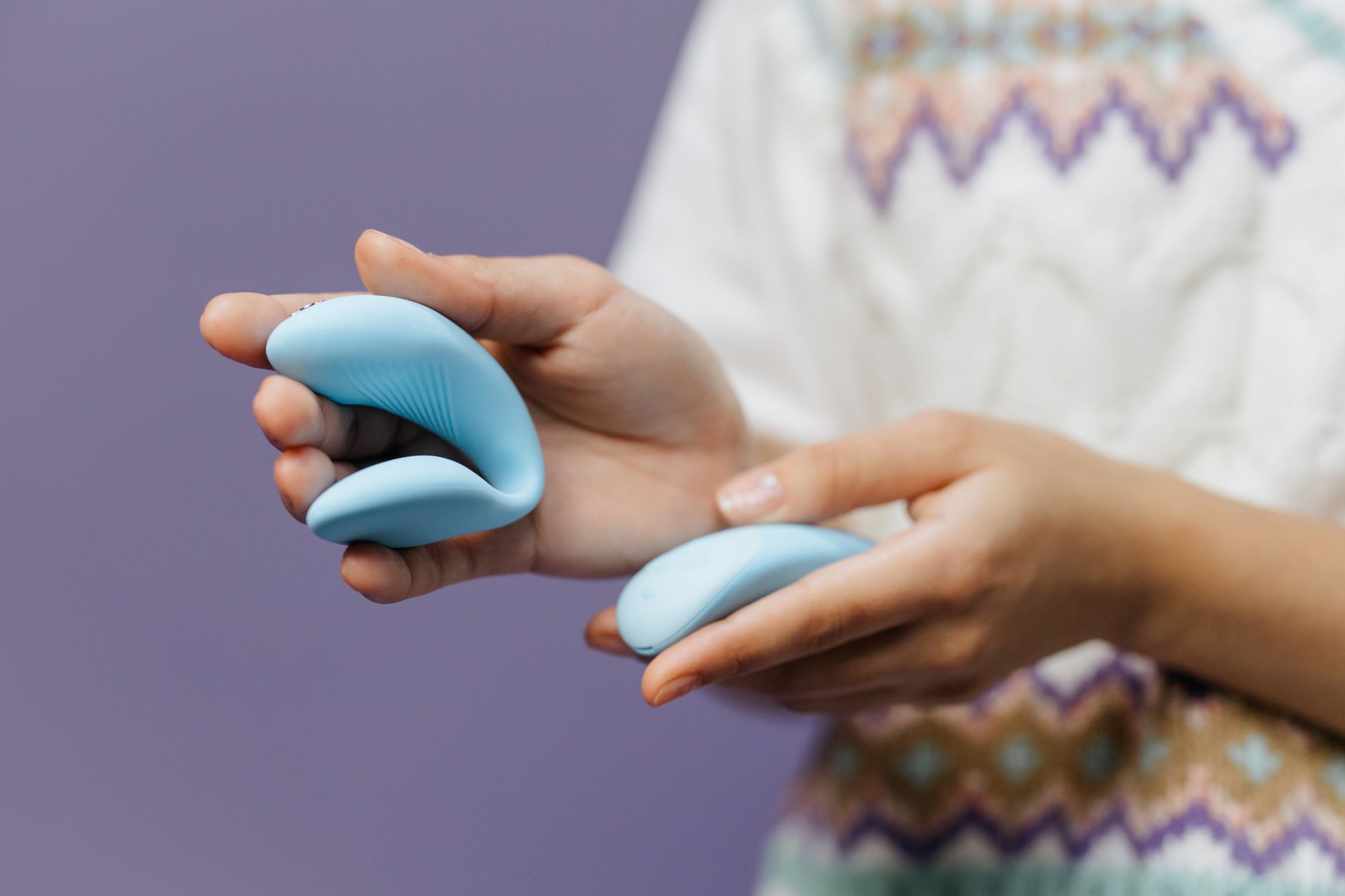 Close-up of hands holding a sleek lemon vibrator against a purple background.