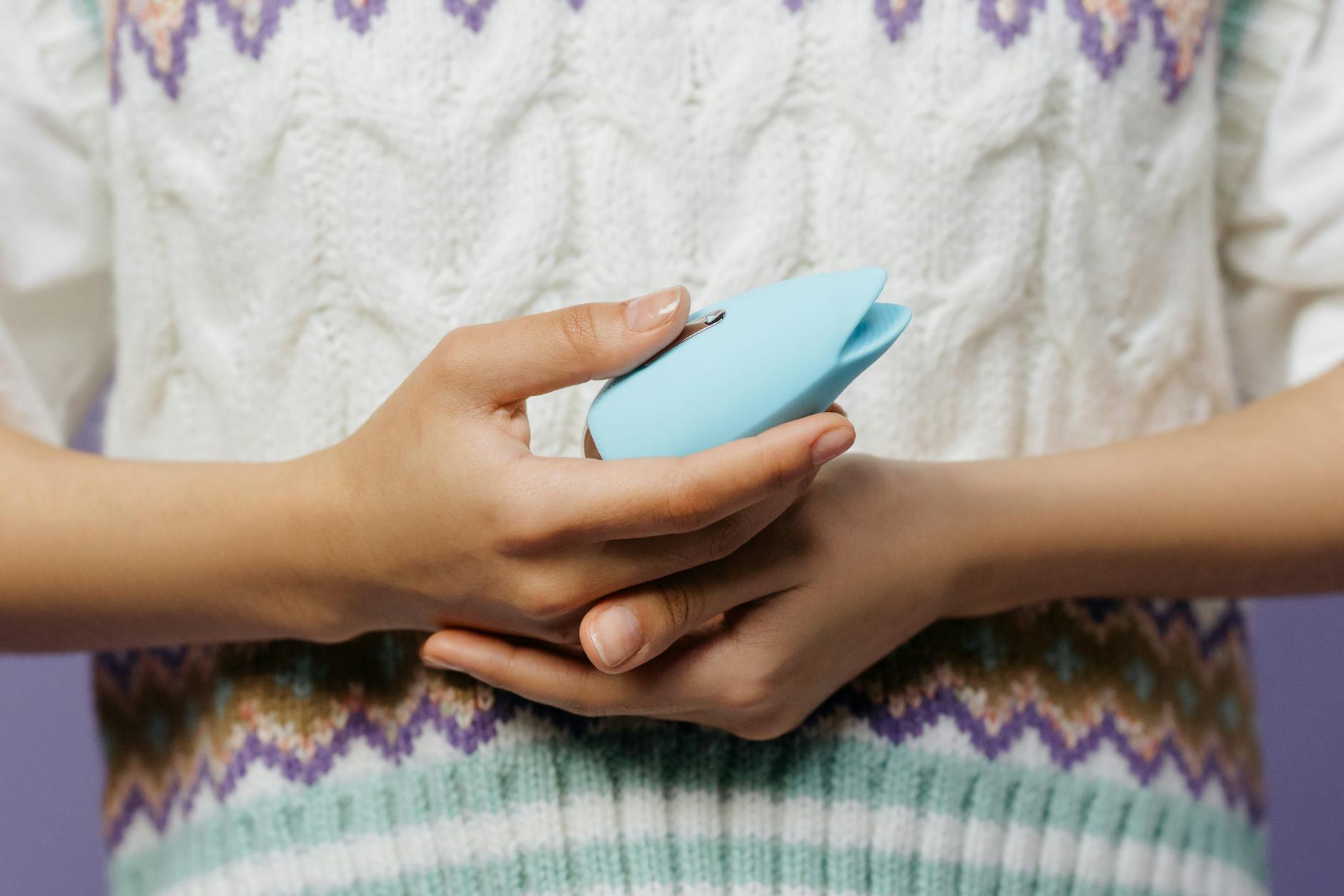 Woman holding a blue personal massager against a knitted sweater, representing gentle clitoral stimulation.